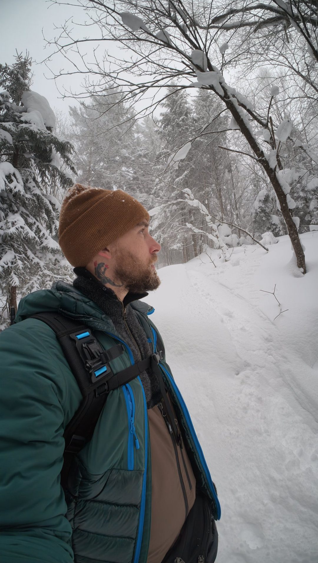 Nick Griffin, founder of By Your Side Outfitters, on a snow-covered trail in a green insulated jacket and brown beanie, looking out over a winter forest