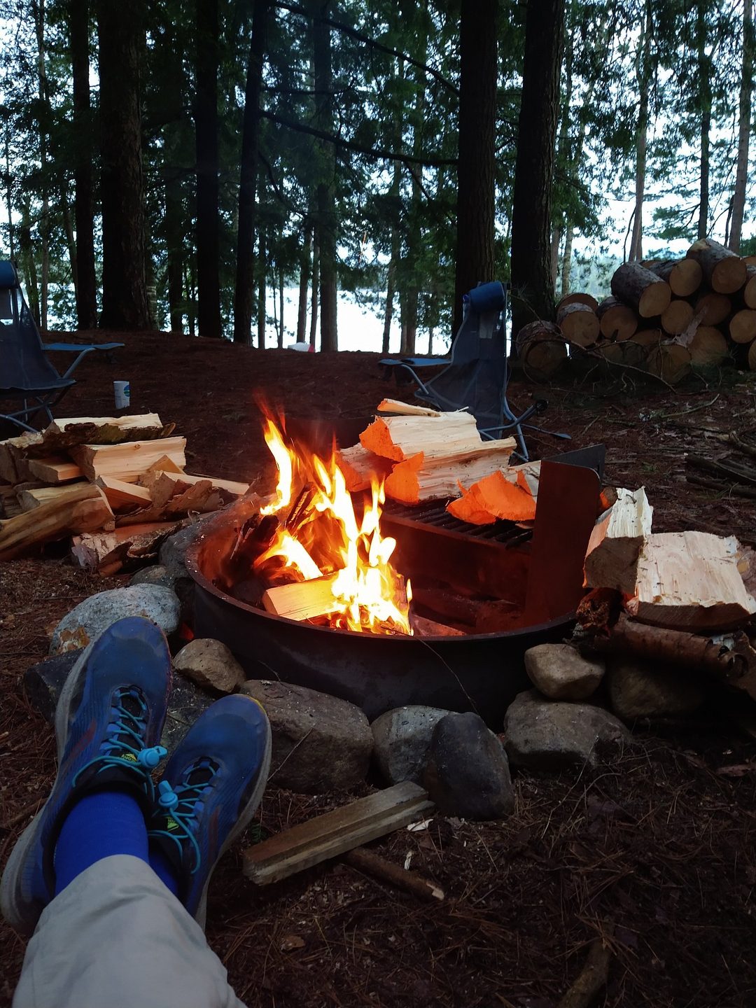 Feet in blue trail shoes resting by a campfire in the pines at dusk