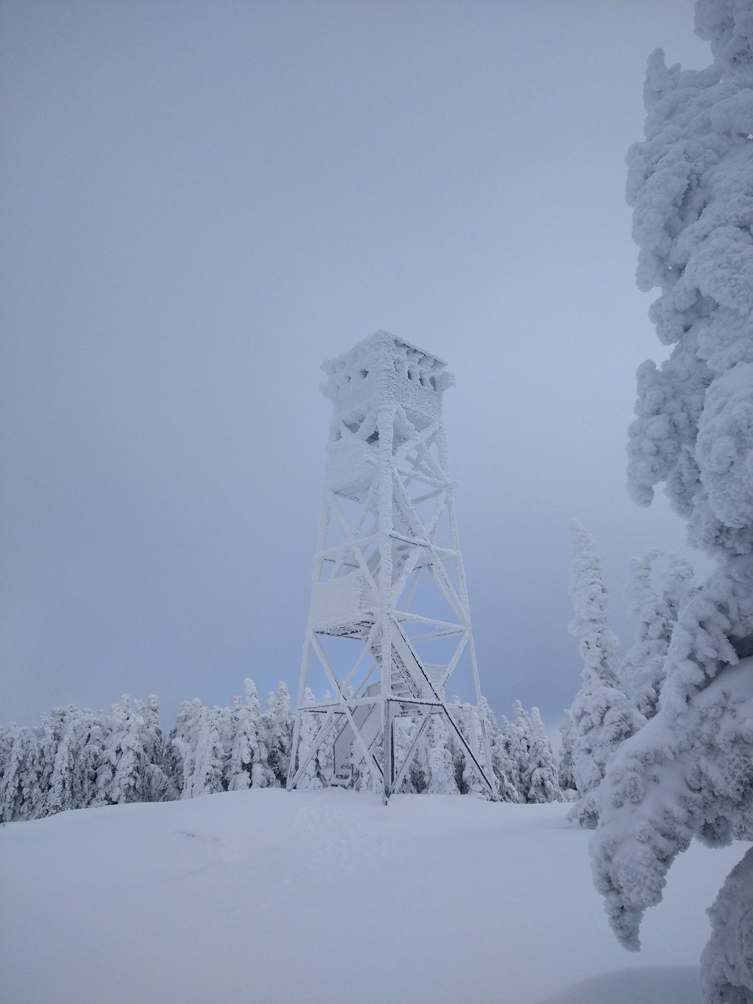 A fire tower completely coated in snow and rime ice under a pale winter sky